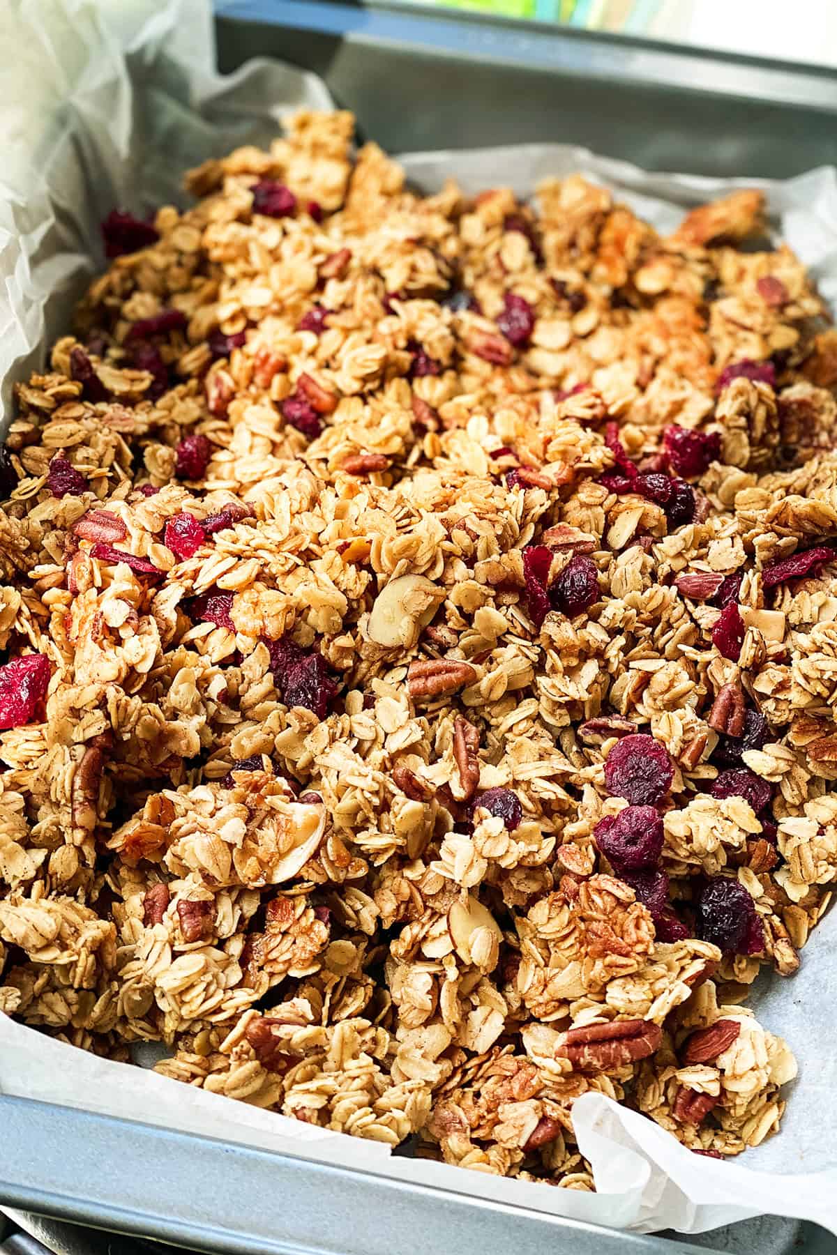 Healthy granola with dried cranberries on a parchment lined baking sheet cooling.