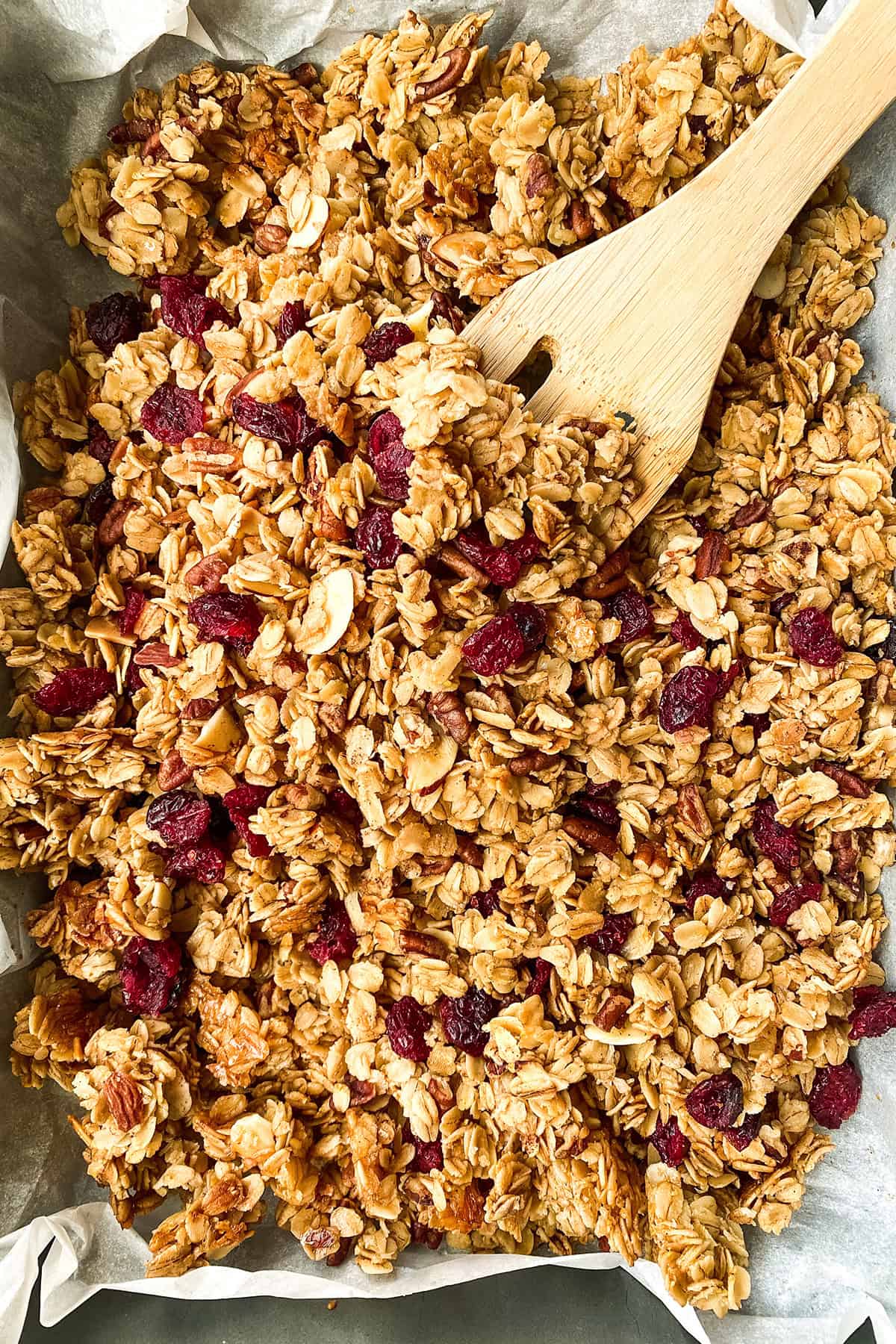 Top view of healthy granola with cranberries and sliced almonds, being stirred on a sheetpan.