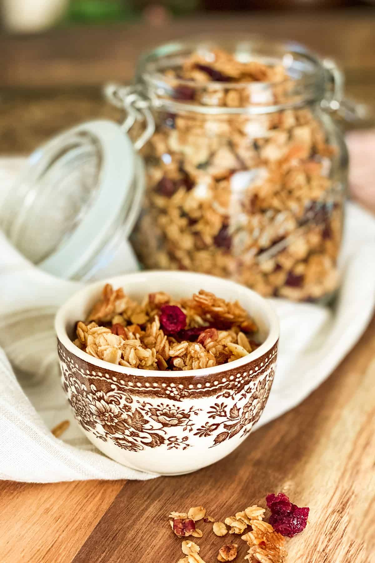 Healthy granola in a brown and white mug with more in a glass lidded jar for storing.