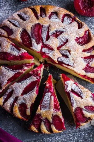 Top view of partially sliced plum cake with a silver server and visible plum slices.