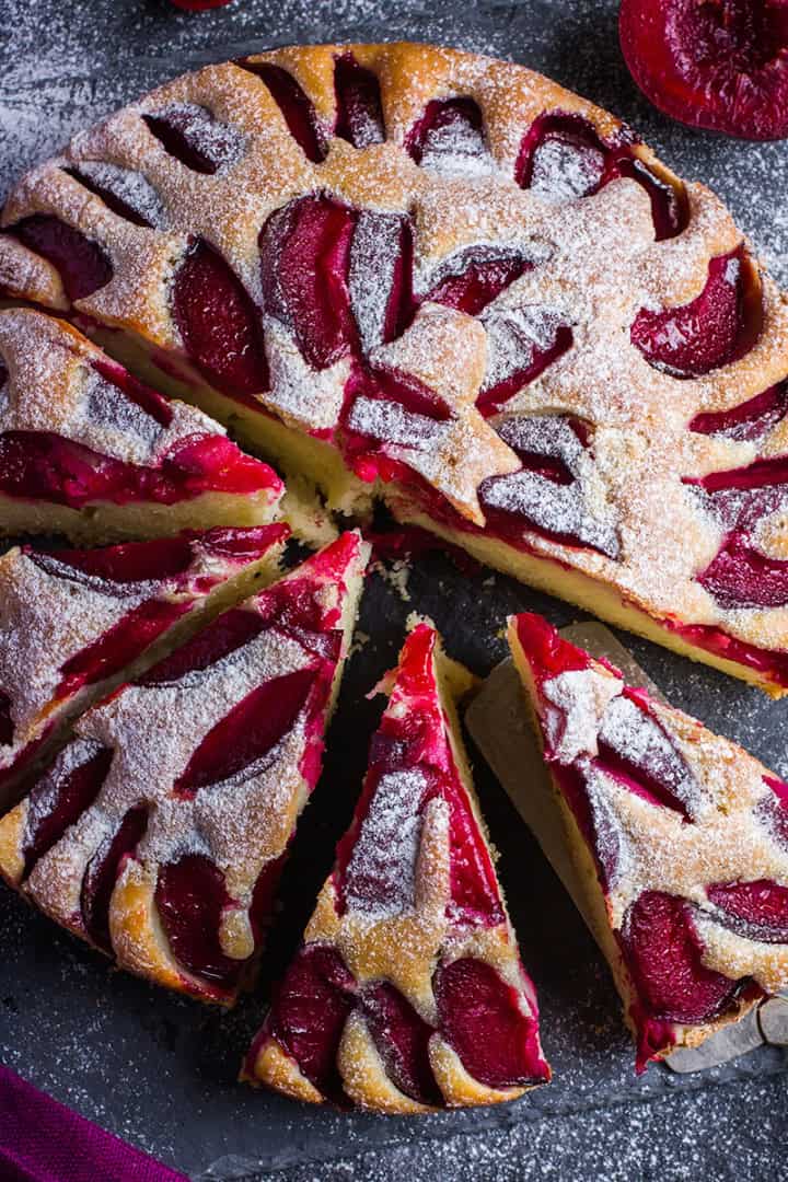 Top view of partially sliced plum cake with a silver server and visible plum slices.