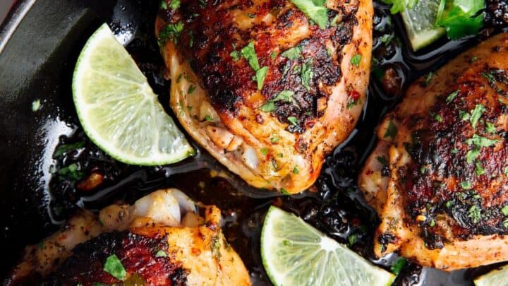 Four seasoned, pan-seared chicken thighs in a skillet with lime wedges and cilantro garnish—a perfect choice for budget friendly dinner recipes.
