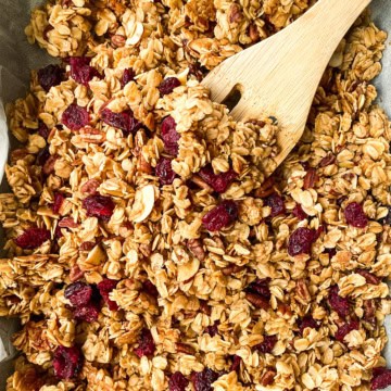 Baked healthy granola with dried fruit in a sheet pan with a wooden spoon, cooling.