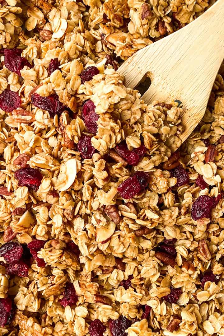 Baked healthy granola with dried fruit in a sheet pan with a wooden spoon, cooling.
