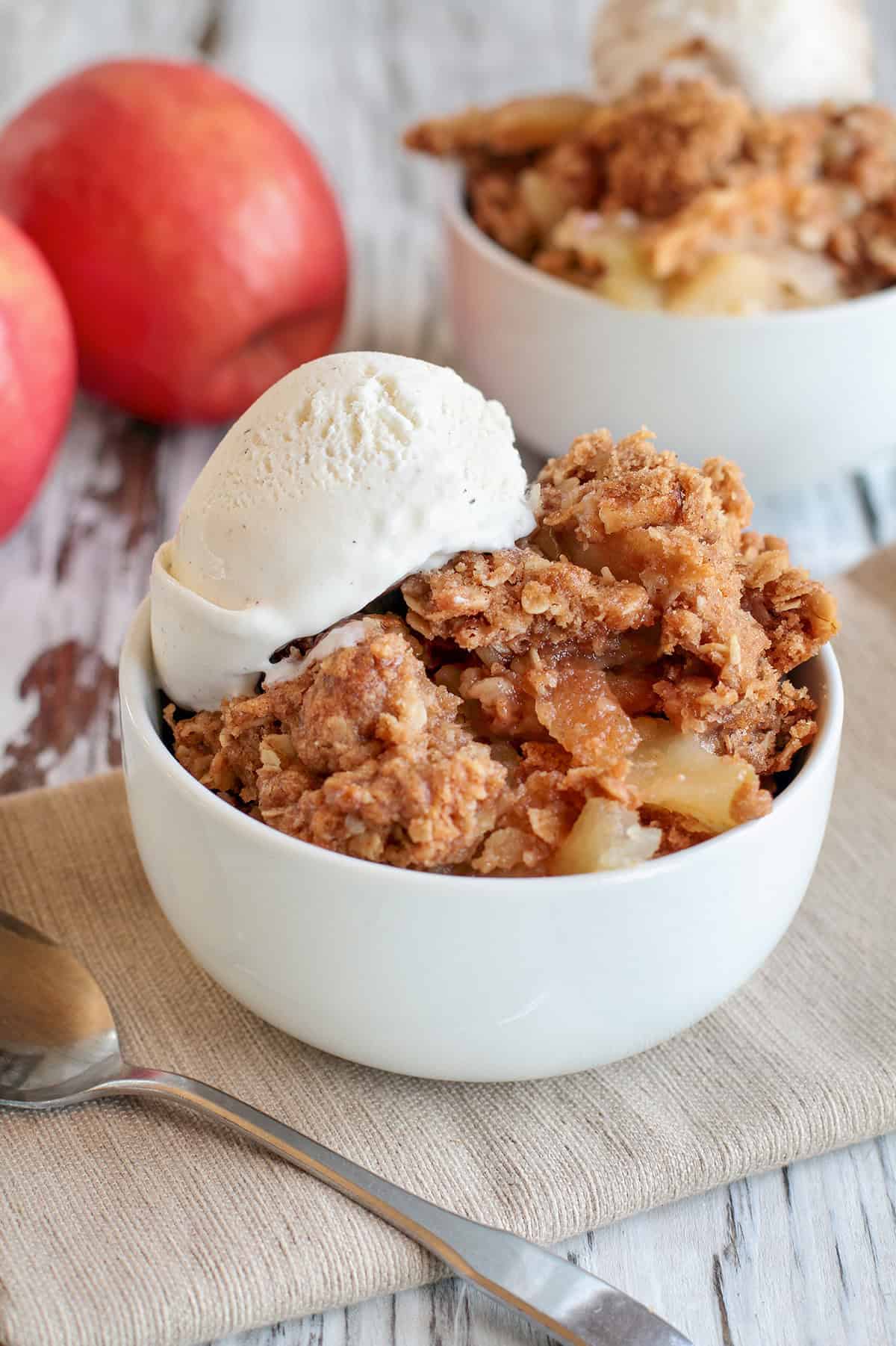 Vertical view of apple crumble serving in a bowl with a scoop of vanilla ice cream on top.