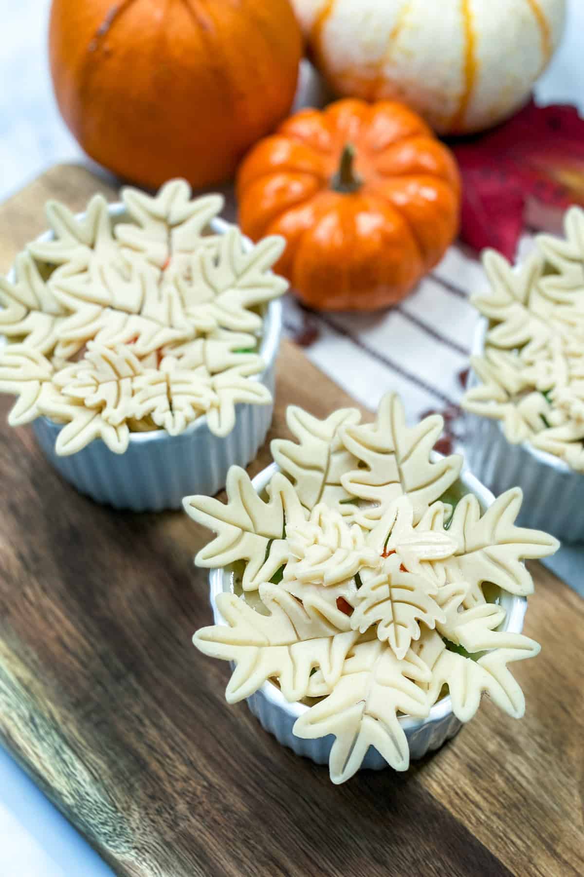 Unbaked mini turkey pot pies, topped with leaf shaped pastry, and ready for the oven.