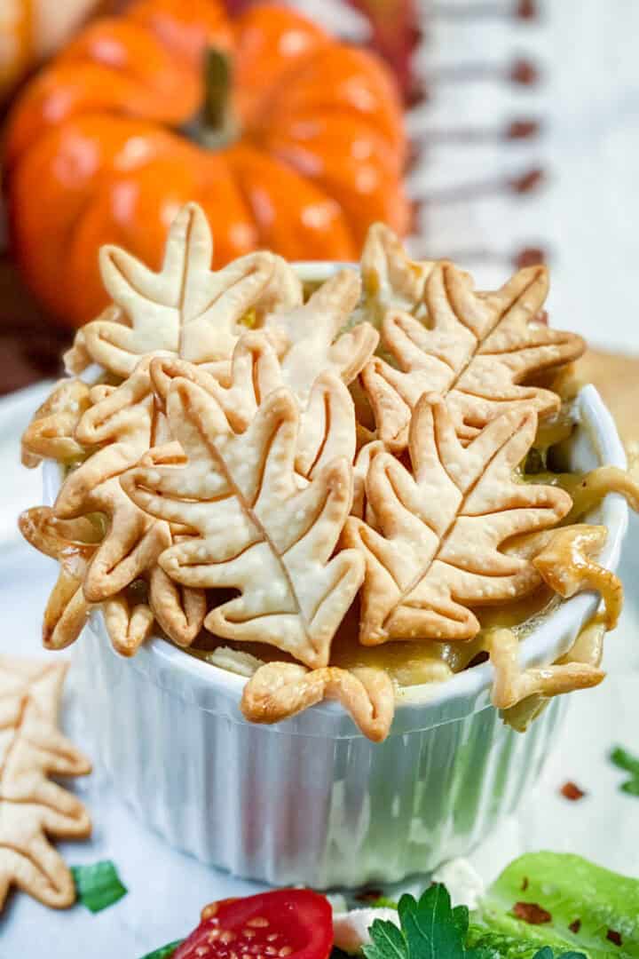 Individual serving of chicken pot pie in a ramekin and topped with fall leaf shaped pie crusts.