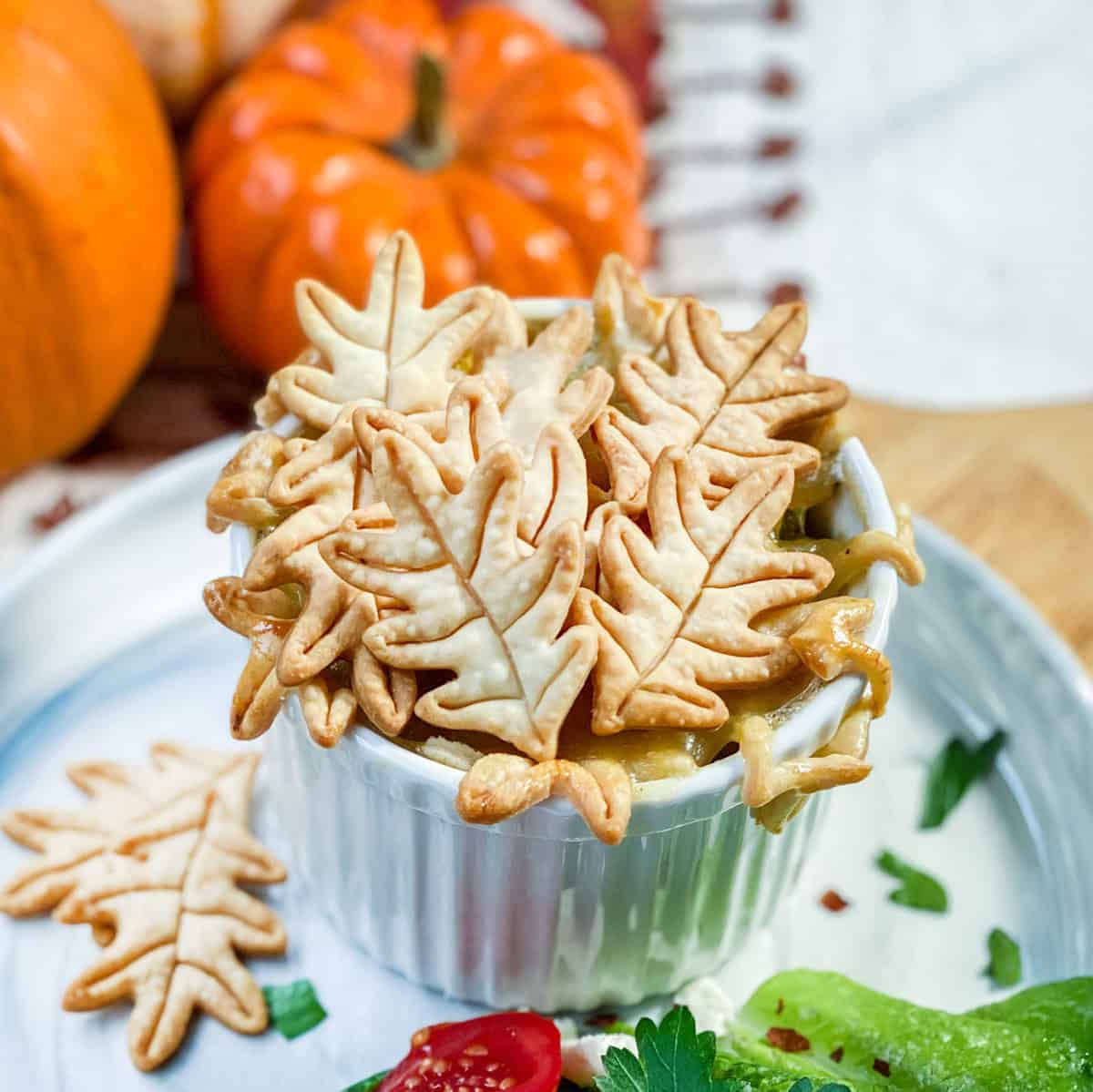 Individual serving of chicken pot pie in a ramekin and topped with fall leaf shaped pie crusts.