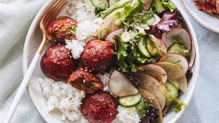 A plate of white rice topped with plant-based meatballs, mixed green salad with sliced cucumber and radish—perfect for quick and cozy Fall 30 Minute Dinners—served with a fork on the side.