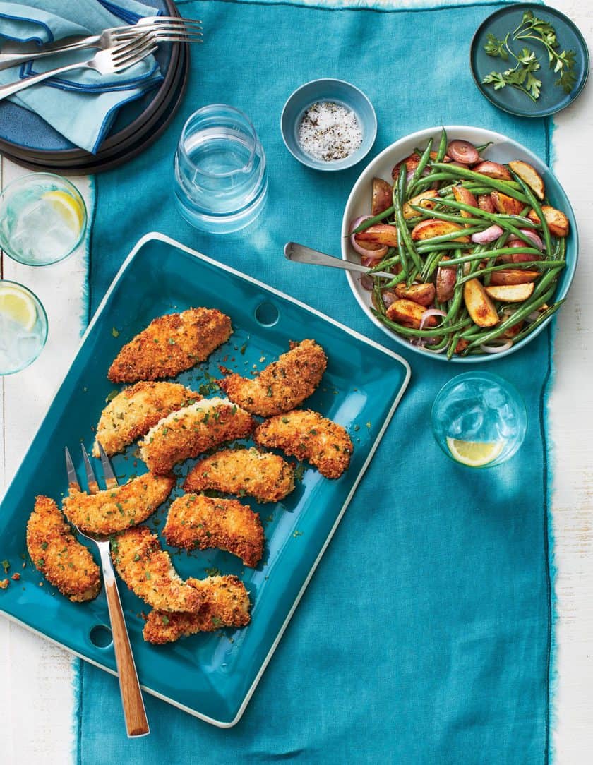 A blue tray with breaded chicken tenders and a bowl of green beans with potatoes on a teal tablecloth-an easy, family-friendly meal perfect for Back to School Dinner Recipes, complete with plates, glasses, and seasonings.