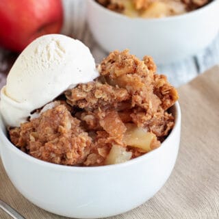 Closeup view of apple crisp with vanilla ice cream in a white bowl