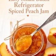 Open jar of peach jam with a spoon, surrounded by sliced peaches on a white wooden surface. Text above reads: "Easy Small Batch Refrigerator Peach Jam with warming spices.