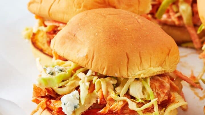 Three chicken sandwiches on a plate, topped with coleslaw and blue cheese crumbles, served on soft buns—perfect for cozy November dinners.