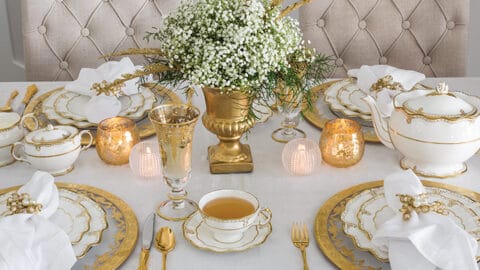 Christmas tea placesetting with gold and white scalopped plates and a centerpiece arrangements of baby's breath flowers in a gold vase.