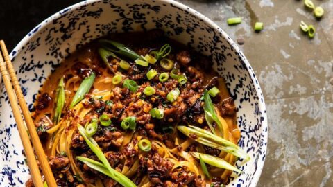 Two bowls of noodles topped with minced meat, sliced green onions, and chili oil, served with chopsticks. Perfect for October Savory Dinners, with a small dish of chopped green onions and extra chili oil on the side.