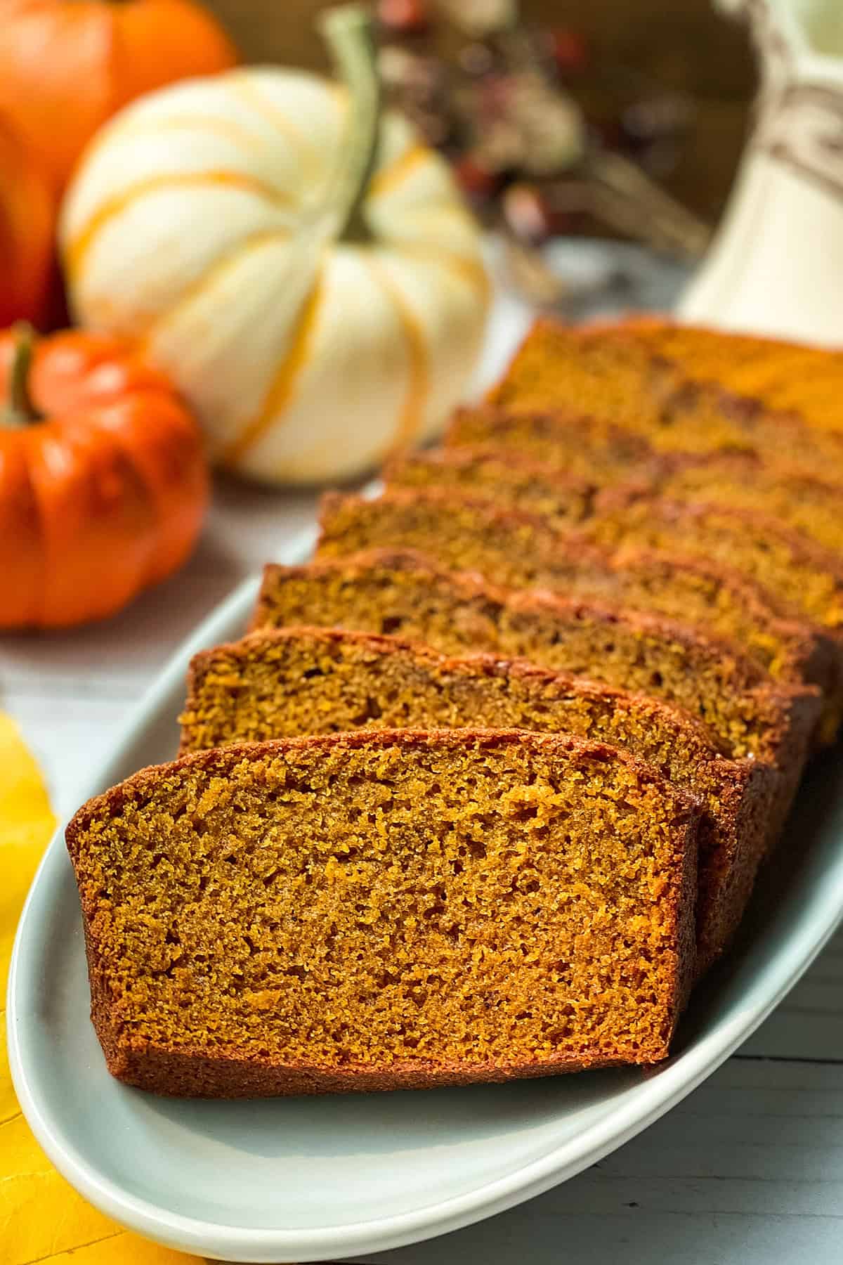Pumpkin bread loaf sliced and arranged on a white platter, surrounded by small decorative pumpkins.
