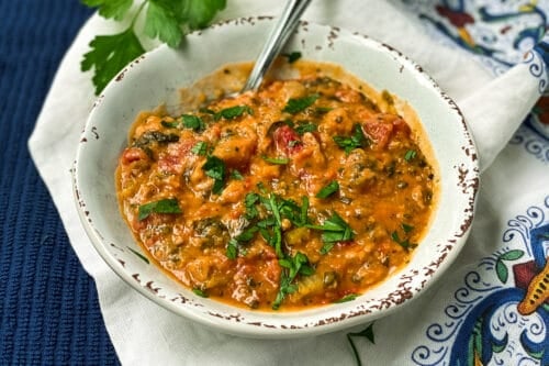 Bowl of Instant Pot Lentil Soup with Sausage and Spinach on a Blue Background