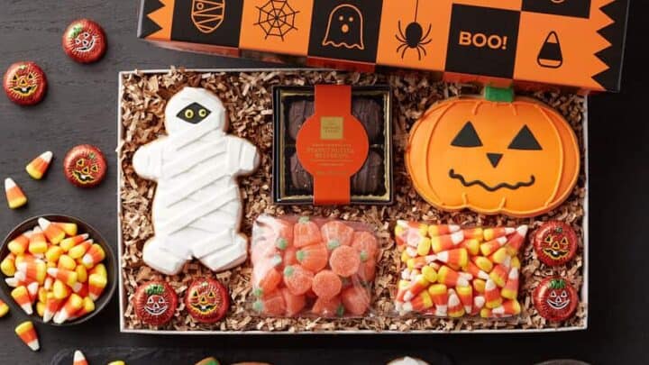 An open Halloween-themed gift box filled with Spooky Halloween Treats—mummy and pumpkin cookies, gummy candies, candy corn, and chocolate candies—all wrapped in festive orange and black packaging.