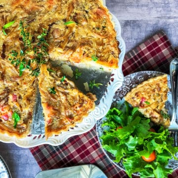 Sliced French Onion Tart on a serving pedestal with a slice on a nearby plate with tossed salad.