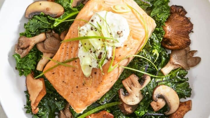A plate of cooked salmon topped with a dollop of sauce and chives, served over saut&eacute;ed kale and mushrooms&mdash;perfect for healthy fall dinners.