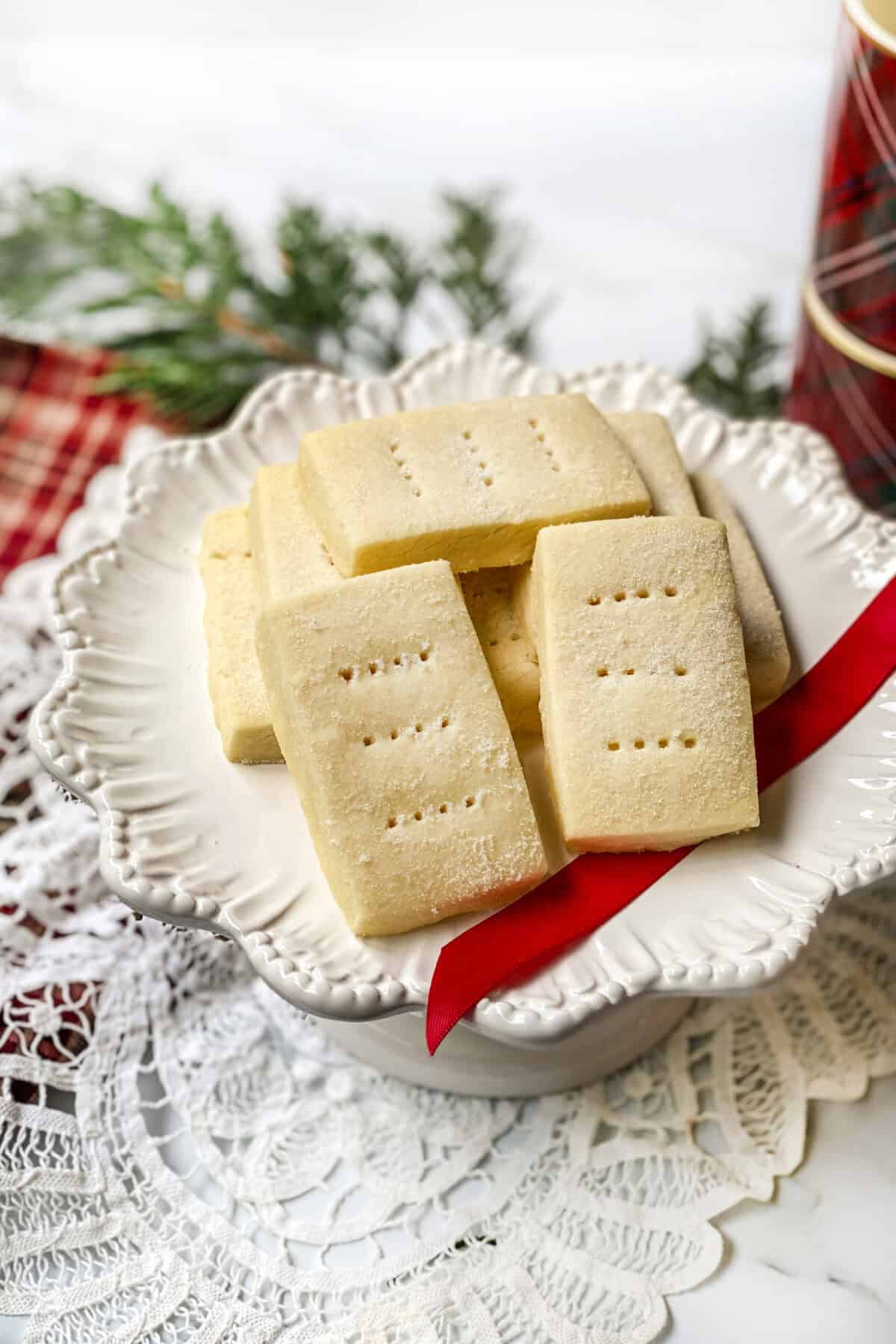 Buckingham Palace shortbread fingers arranged on a white plate with sanding sugar, holiday greenery, and plaid napkin.