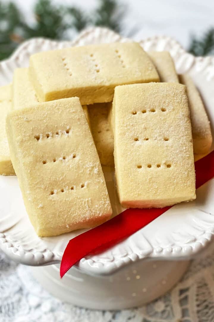Close-up of Buckingham Palace shortbread cookies stacked on a white pedestal plate with sanding sugar and fork marks.