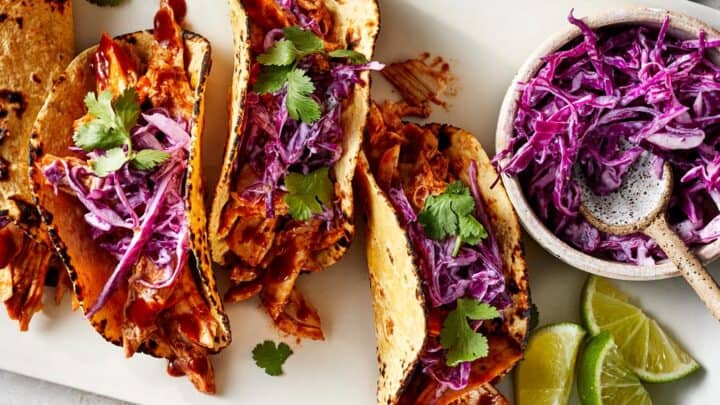 Enjoy these Healthy 15 Minute Dinners: three shredded chicken tacos topped with purple cabbage slaw and cilantro, served with lime wedges and extra slaw on the side.