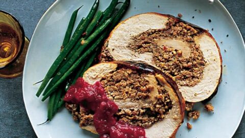 A plate with two slices of stuffed turkey breast topped with cranberry sauce, green beans on the side, and two drinks partially visible—a perfect Small Thanksgiving Dinner.