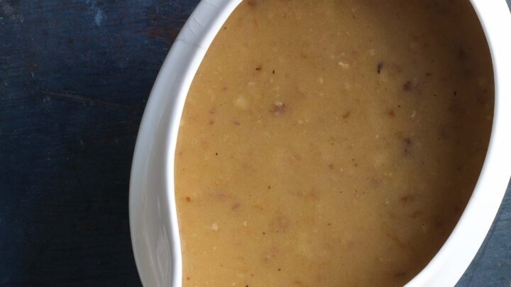 A white gravy boat filled with brown gravy, perfect for a small Thanksgiving dinner, placed on a dark blue surface.