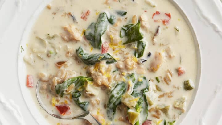 A bowl of creamy soup containing leafy greens, diced vegetables, and chunks of meat, with a spoon resting in the bowl—perfect for healthy 20 minute dinners.