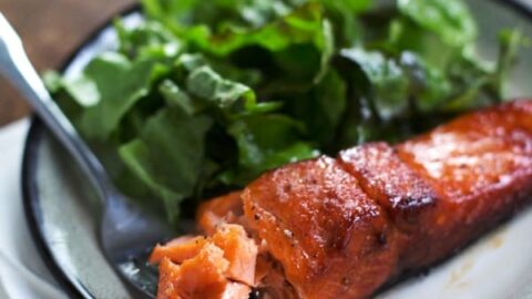 A plate with a piece of cooked salmon and a serving of leafy green salad, perfect for easy 5 Ingredient Fall Dinners, set on a wooden table with a white napkin and a fork.
