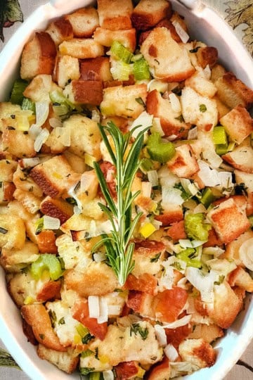 Top view of classic stuffing recipe in an oval ceramic baking dish and garnished with a rosemary sprig.