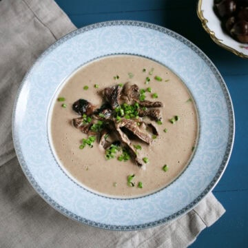 Bowl of creamy chestnut mushroom soup in a blue bowl and garnished with sauteed mushrooms and fresh herbs.