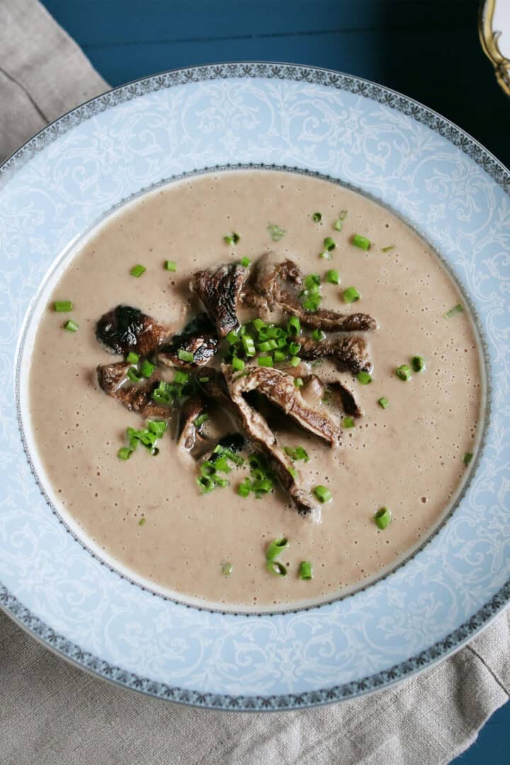 Bowl of creamy chestnut mushroom soup in a blue bowl and garnished with sauteed mushrooms and fresh herbs.
