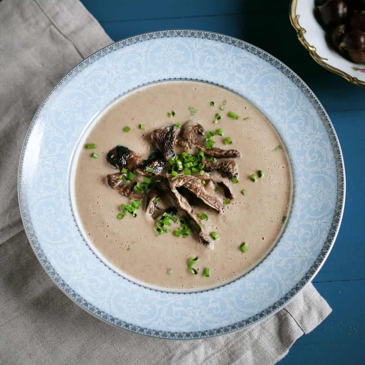 Bowl of creamy chestnut mushroom soup in a blue bowl and garnished with sauteed mushrooms and fresh herbs.