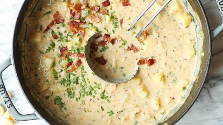 A pot of creamy chowder with potatoes and herbs, topped with chopped bacon—perfect for Christmas Eve recipes. Surrounding the pot are a bowl of oyster crackers, measuring spoons, and a bowl of bacon pieces.