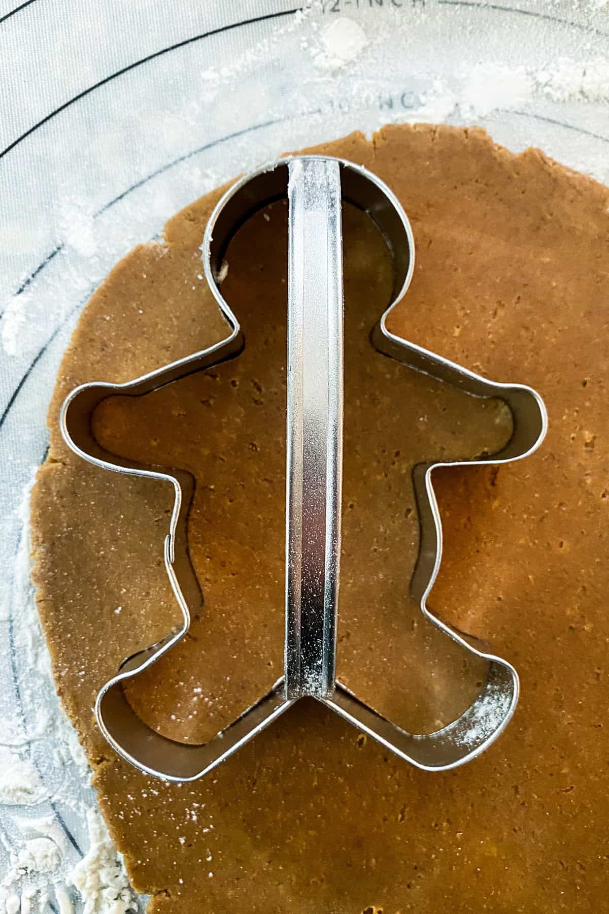 A metal gingerbread person cookie cutter sits on rolled-out dough, ready to create festive gingerbread cookies.