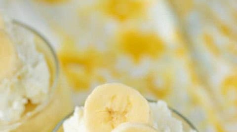 A glass filled with banana pudding, topped with whipped cream and banana slices, sits on a marble surface—perfect for your 12 Days of Christmas Recipes collection.