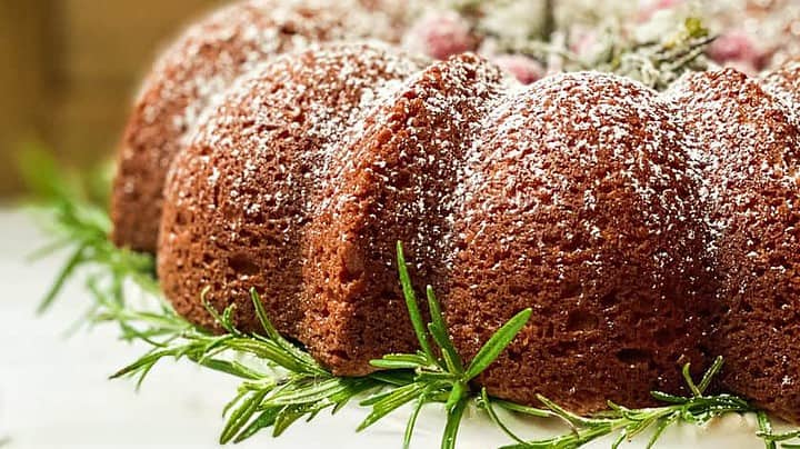 Closeup view of Spiced Christmas Cake on a white cake stand decorated with fresh rosemary and sugared cranberries.