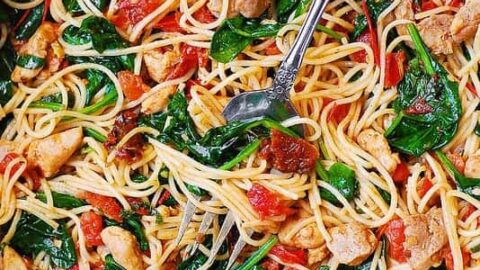 A skillet filled with spaghetti, cooked chicken pieces, spinach, and diced tomatoes—perfect for healthy 20 minute dinners. A serving fork and spoon are ready for a quick, delicious meal.