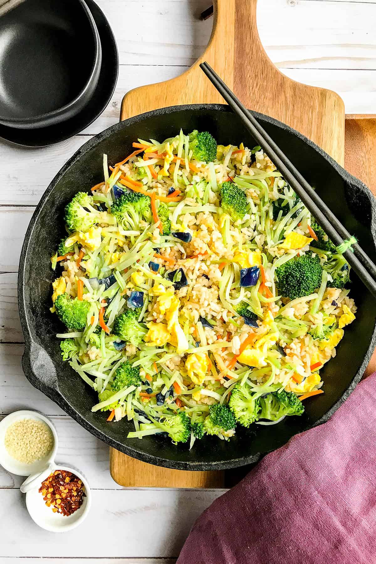 Top view of broccoli cabbage fried rice in a cast iron skillet with a bowl nearby for serving.