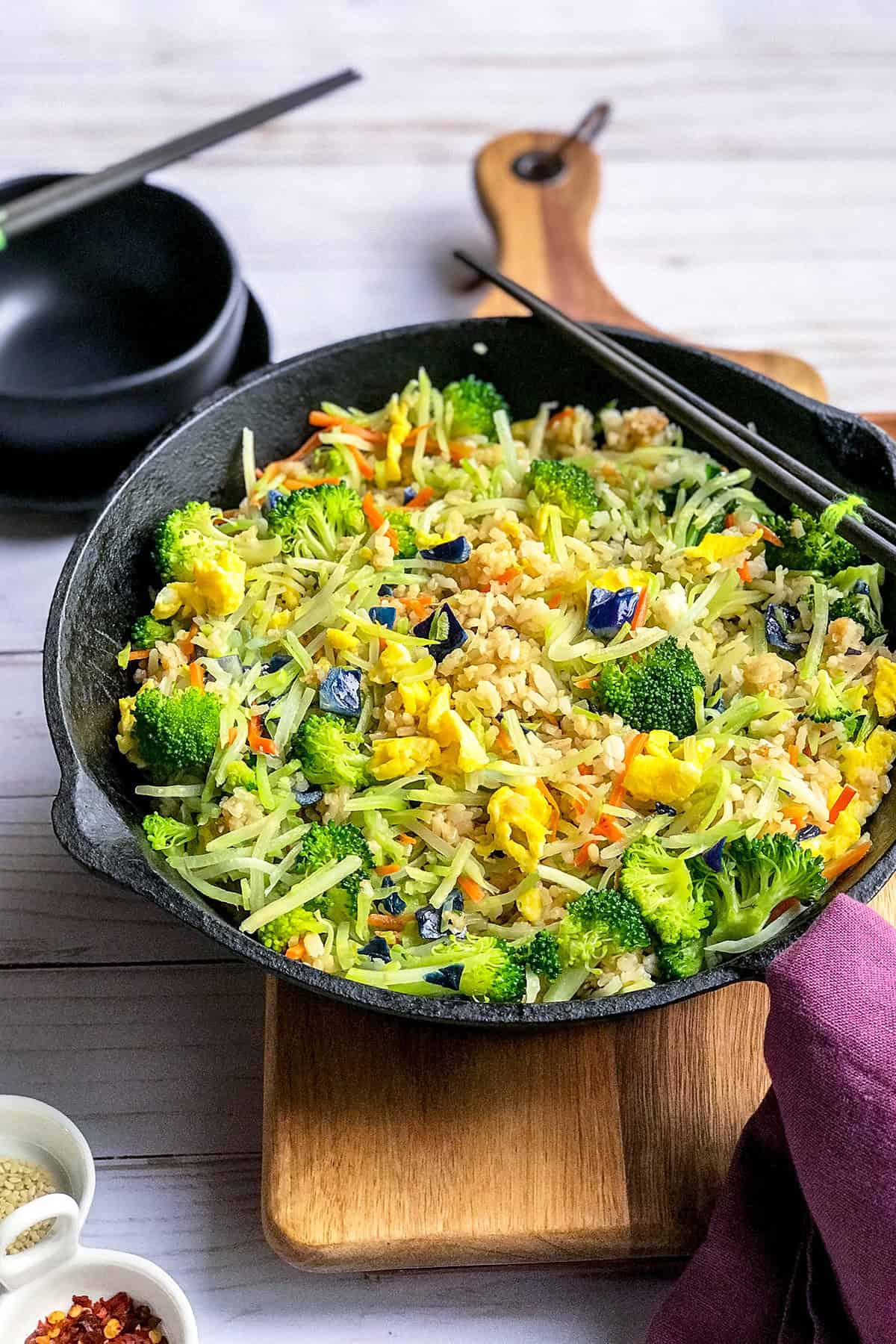 Side view of Broccoli Cabbage Fried Rice in a cast iron skillet with chop sticks resting on the side of the skillet.