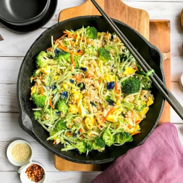 Top view of coleslaw fried rice in a cast iron skillet with chop sticks resting on the side and red pepper flakes nearby.