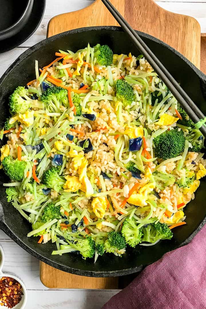Top view of coleslaw fried rice in a cast iron skillet with chop sticks resting on the side and red pepper flakes nearby.