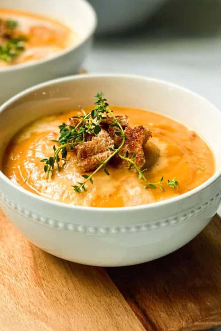 Bowl of creamy root vegetable soup in a bowl and garnished with toasted croutons and fresh thyme.