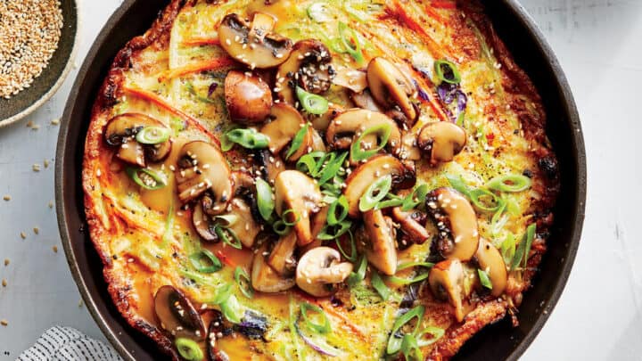 A cooked omelette topped with sautéed mushrooms, sliced green onions, and sesame seeds, served in a black pan on a white surface—perfect for quick and satisfying 400 Calorie Dinners.