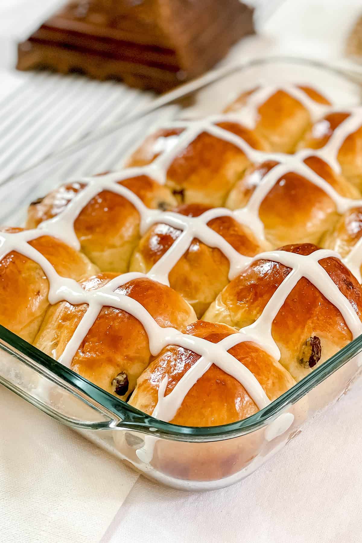 A glass baking dish filled with golden brown hot cross buns, each topped with white icing crosses-perfect for trying your favorite hot cross buns recipe.