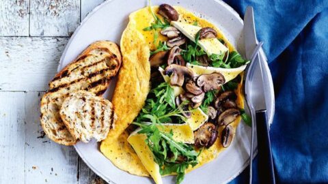 Mushroom filled omelet on a white plate with sliced bread.