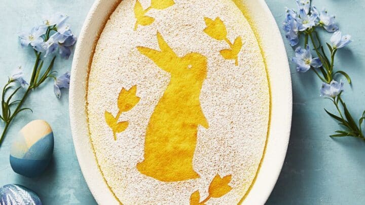 Top view of lemon pudding cake with an Easter bunny stenciled on top using powdered sugar over a pastel blue background.