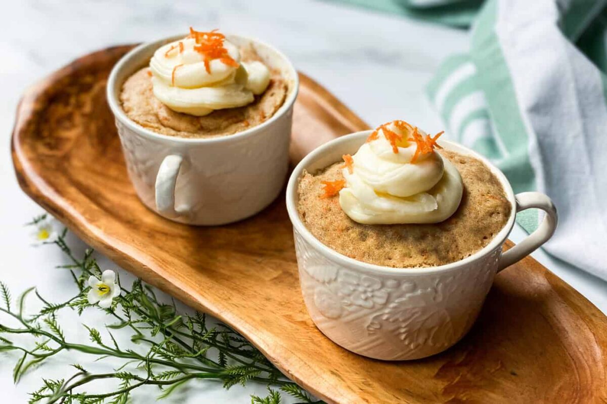 2 Carrot Cake Mug Cakes Topped with Whipped Cream Cheese on a Wood Serving Board